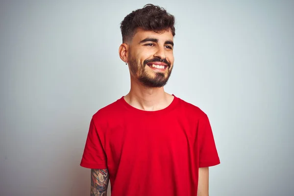 赤いTシャツを着た若い男は 顔に笑顔で横を向いて 孤立した白い背景の上に立って 自然な表情 自信を持って笑う — ストック写真