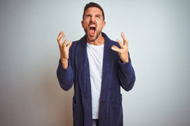 Genç adam rahat pijama ve cüppe giyen sabah izole arka plan deli ve deli bağırarak ve agresif ifade ve kollar kaldırdı ile bağırıyor. Hayal kırıklığı kavramı.