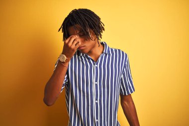 Izole sarı arka plan yorgun burun ve gözler yorgunluk ve baş ağrısı hissi üzerinde rahat çizgili t-shirt giyen dreadlocks ile Afro adam. Stres ve hayal kırıklığı kavramı.