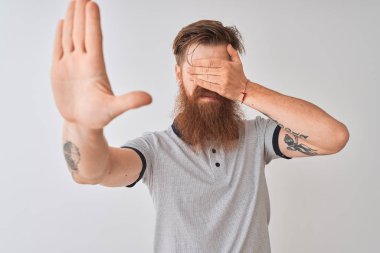 Genç kızıl İrlandalı adam elleri ile gözleri kaplayan izole beyaz arka plan üzerinde duran gri polo giyen ve üzgün ve korku ifade ile stop jest yapıyor. Utanmış ve olumsuz kavram.