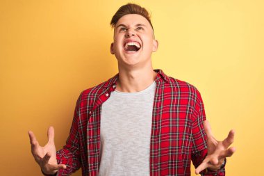 Genç yakışıklı adam izole sarı arka plan deli ve deli bağırarak ve agresif ifade ve kollar kaldırdı ile bağırıyor üzerinde duran rahat gömlek giyiyor. Hayal kırıklığı kavramı.