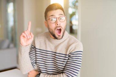 Evde gözlük takan genç yakışıklı adam başarılı bir fikirle parmağını yukarı yasladı. Çıktı ve mutlu. Bir numara.