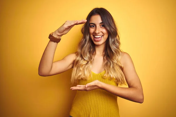 Young beautiful woman wearing t-shirt over yellow isolated background gesturing with hands showing big and large size sign, measure symbol. Smiling looking at the camera. Measuring concept.