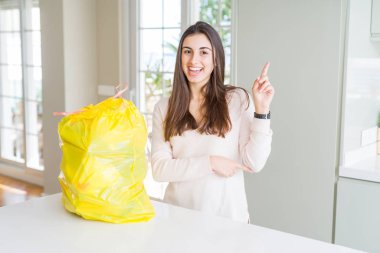Güzel genç kadın yüzünde büyük bir gülümseme ile çöp konteyner dışarı alarak, kameraya bakarak yan el ve parmak ile işaret.
