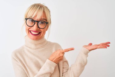 Izole beyaz arka plan üzerinde boğazlı kazak ve gözlük giyen orta yaş kadın şaşırttı ve el ile sunarken kameraya gülümseyerek ve parmak ile işaret.