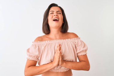 Genç güzel kadın rahat t-shirt izole beyaz arka plan üzerinde ayakta yalvarıyor ve elleri ile birlikte umut ifadesi ile dua yüz çok duygusal ve endişeli. Af dilemek istiyorum. Din kavramı.