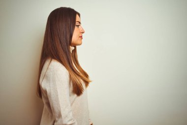 Yan bakan izole beyaz arka plan üzerinde kış boğazlı kazak giyen genç güzel kadın, kendine güvenen gülümseme ile doğal yüz ile profil poz rahatlayın.