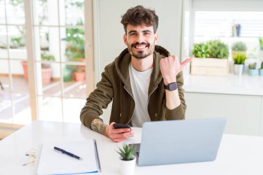 Akıllı telefon kullanarak ve dizüstü bilgisayar kullanarak eğitim genç öğrenci adam işaret ve mutlu yüzü gülümseyerek yan başparmak ile gösteren