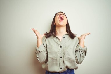 Genç güzel esmer kadın izole arka plan deli ve deli bağırarak üzerinde yeşil gömlek giyen ve agresif ifade ve kollar kaldırdı ile bağırıyor. Hayal kırıklığı kavramı.