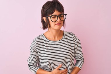 Genç güzel kadın çizgili t-shirt ve gözlük giyen mide üzerinde el ile izole pembe arka plan üzerinde mide, ağrılı hastalık kötü hissediyorum. Ağrı kavramı.