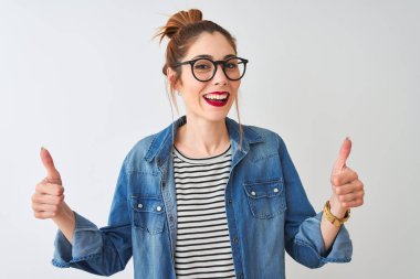 Redhead woman wearing striped t-shirt denim shirt and glasses over isolated white background success sign doing positive gesture with hand, thumbs up smiling and happy. Cheerful expression and winner gesture.