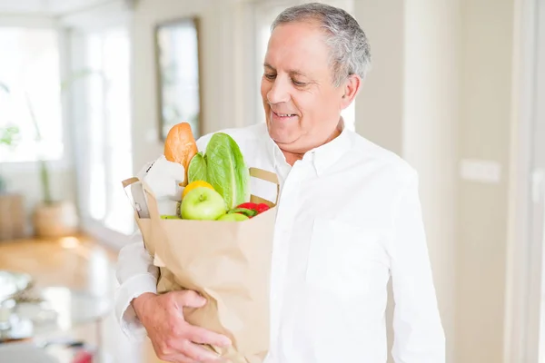 Handsome senior man holding paper bag full of fresh groceries an