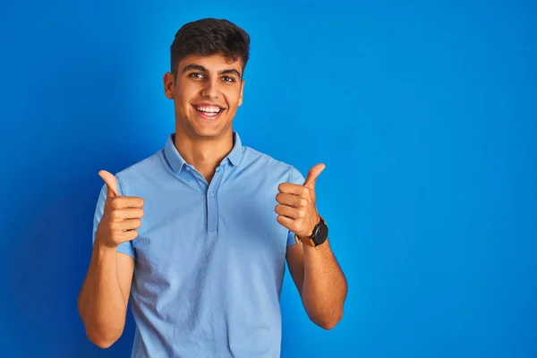年轻的印度男子穿着休闲马球站在孤立的蓝色背景成功标志做积极的姿态与手 竖起大拇指微笑和快乐 欢快的表情和获胜的手势 — 图库照片
