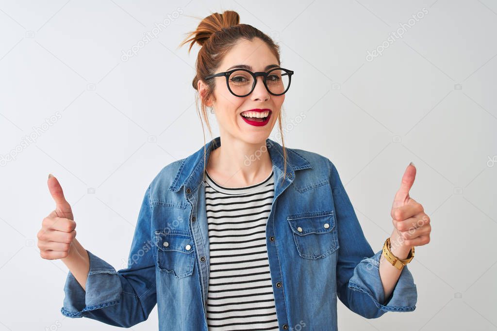 Redhead woman wearing striped t-shirt denim shirt and glasses over isolated white background success sign doing positive gesture with hand, thumbs up smiling and happy. Cheerful expression and winner gesture.