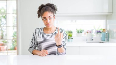 Afro saçlı, sıradan çizgili süveter giyen, orta parmağını gösteren, kaba ve kaba bir ifade sergileyen güzel Afro-Amerikalı kadın.