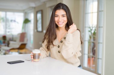 Genç kadın evde bir fincan kahve içerken gururla bağırArak ve zafer ve başarıyı kutlayan çok heyecanlı, tezahürat duygu