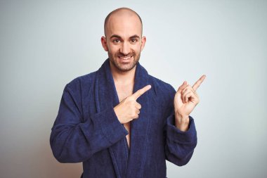 Mavi bornoz giyen genç adam, izole arka plan üzerinde rahat bir yaşam tarzı gülümseyerek ve yan iki el ve parmak ile işaret kamera bakıyor.