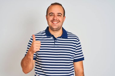Izole beyaz arka plan üzerinde duran rahat çizgili polo giyen genç adam el ile jest kadar mutlu başparmak yapıyor. Başarı gösteren kameraya bakarak ifadeyi onaylama.