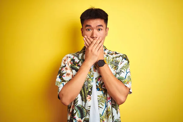 Asian chinese man on holiday wearing summer shirt over isolated yellow background shocked covering mouth with hands for mistake. Secret concept.
