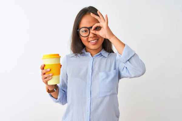 Young chinese woman wearing glasses holding glass of coffee over isolated white background with happy face smiling doing ok sign with hand on eye looking through fingers