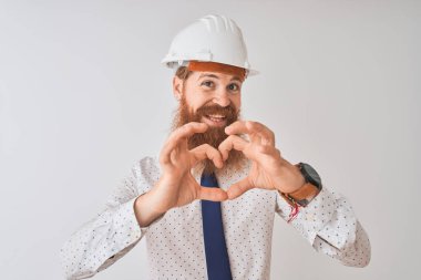 Genç kızıl İrlandalı mimar adam izole beyaz arka plan üzerinde güvenlik kask giyen aşk elleri ile kalp sembolü şekli yapıyor gülümseyerek. Romantik kavram.