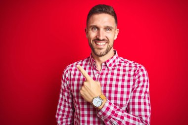 Kırmızı izole arka plan neşeli üzerinde genç yakışıklı adam mutlu ve doğal ifade ile yan yana el ve parmak ile işaret yüzünde bir gülümseme ile neşeli