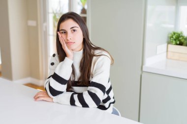 Çizgili kazak giyen güzel genç bir kadın kollarını kavuşturarak depresyondan yorgun ve sıkılmış göründüğünü düşünüyor..