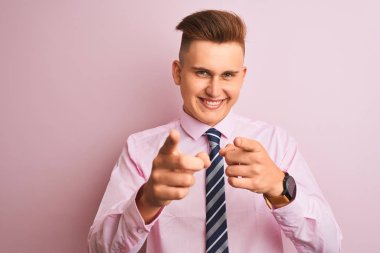 Genç yakışıklı işadamı gömlek ve kravat izole pembe arka plan üzerinde mutlu ve komik yüzü ile kameraya parmaklarını gösteren ayakta giyiyor. İyi enerji ve titreşimler.