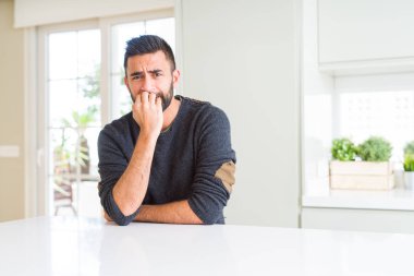 Evde rahat kazak giyen yakışıklı İspanyol adam vurguladı ve ağız ısırma çivi elleri ile gergin bakıyor. Anksiyete sorunu.