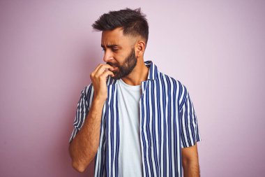 Genç yakışıklı hintli adam izole pembe arka plan üzerinde yaz çizgili gömlek giyen stresli ve ağız tırnak ısırma elleri ile sinirli görünümlü. Anksiyete sorunu.