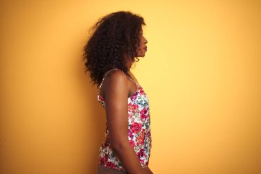 Izole sarı arka plan üzerinde çiçek yazlık t-shirt giyen Afrikalı-Amerikalı kadın yan bakıyor, kendine güvenen gülümseme ile doğal yüzü ile profil poz dinlenmek.