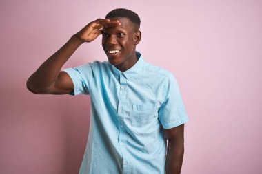 Izole pembe arka plan üzerinde duran mavi rahat gömlek giyen Afrikalı Amerikalı adam çok mutlu ve başının üzerinde el ile uzak görünümlü gülümsüyor. Arama konsepti.