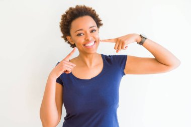 Beyaz arka plan üzerinde genç güzel afro-amerikan kadın güvenle gösteren gülümseyerek ve parmakları diş ve ağız ile işaret. Sağlık kavramı.