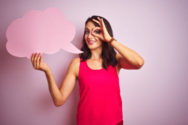 Mutlu yüz ile pembe izole arka plan üzerinde konuşma balonu tutan güzel kadın parmakları ile bakarak göz üzerinde el ile ok işareti yapıyor gülümseyerek