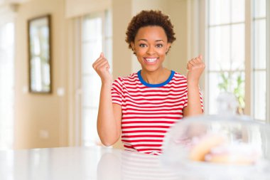 Genç güzel Afrikalı-Amerikalı kadın evde geçirilen silahlarla şaşırmış ve başarı için hayran kutluyor ve gözleri açık. Kazanan kavramı.