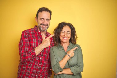 Yüzünde mutlu ve doğal ifade ile yan kadar el ve parmak ile işaret yüz bir gülümseme ile izole sarı arka plan neşeli üzerinde güzel orta yaş çift