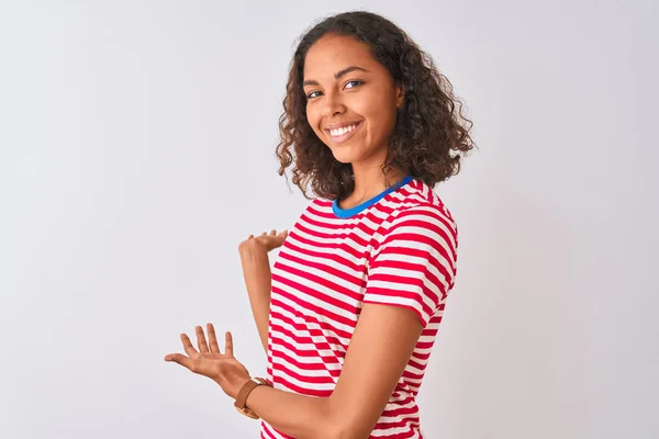 孤立した白い背景の上に立つ赤いストライプのTシャツを着た若いブラジル人女性は 開いた手で自然に微笑み始める — ストック写真