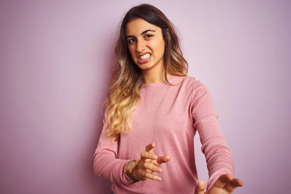 Young beautiful woman wearing a sweater over pink isolated background disgusted expression, displeased and fearful doing disgust face because aversion reaction. With hands raised. Annoying concept.