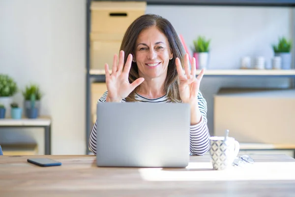 中年老妇人坐在桌旁 在家里用电脑笔记本电脑显示和指着手指9号 同时微笑自信和快乐 — 图库照片