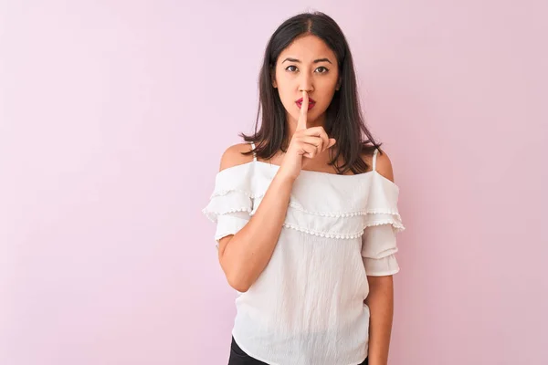 白いTシャツを着た美しい中国人女性は 唇に指で静かにしてほしいと頼む孤立したピンクの背景の上に立っている 沈黙と秘密の概念 — ストック写真