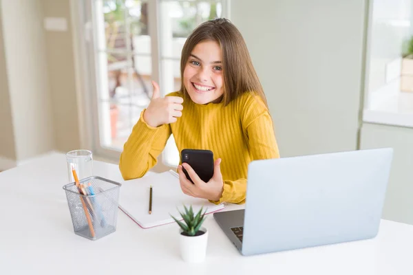美丽的年轻女孩孩子使用智能手机和电脑笔记本电脑快乐与大微笑做Ok标志 拇指用手指 优秀的标志 — 图库照片