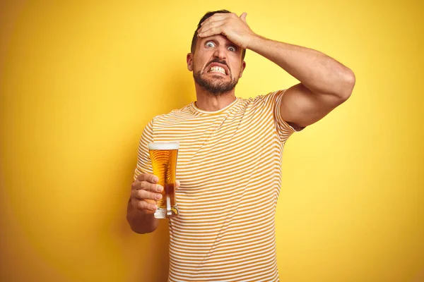 孤立した黄色の背景の上にビールのパイントグラスを飲む若いハンサムな男は 頭の上に手で強調し 恥と驚きの顔でショックを受け 怒りとイライラしました 間違いに対する恐怖と動揺 — ストック写真