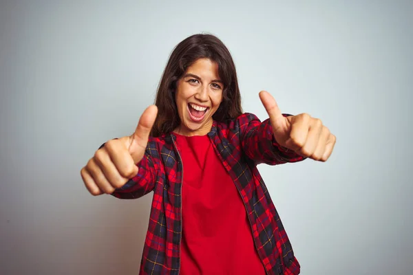 Young beautiful woman wearing red t-shirt and jacket standing over white isolated background approving doing positive gesture with hand, thumbs up smiling and happy for success. Winner gesture.