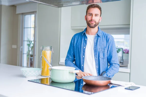 Yakışıklı adam yüzünde ciddi bir ifade ile mutfakta İtalyan spagetti makarna pişirme. Kameraya basit ve doğal bir bakış.