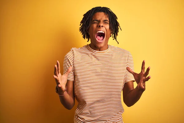 Dreadlocks çizgili t-shirt giyen Afro adam izole sarı arka plan üzerinde ayakta silah kaldırdı ve kapalı gözleri ile başarı için deli ve deli kutluyor heyecanlı çığlık. Kazanan kavramı