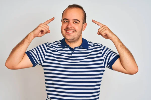 Izole beyaz arka plan üzerinde duran rahat çizgili polo giyen genç adam her iki eliyle parmak, harika bir fikir ya da düşünce, iyi bellek ile baş gösteren gülümseyerek