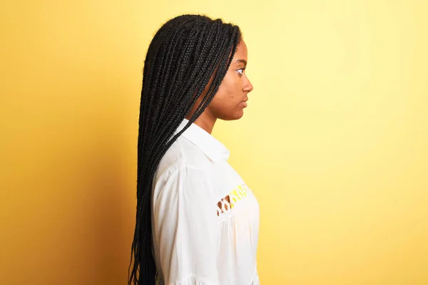 African american woman on vacation wearing bikini and shirt over isolated yellow background looking to side, relax profile pose with natural face with confident smile.