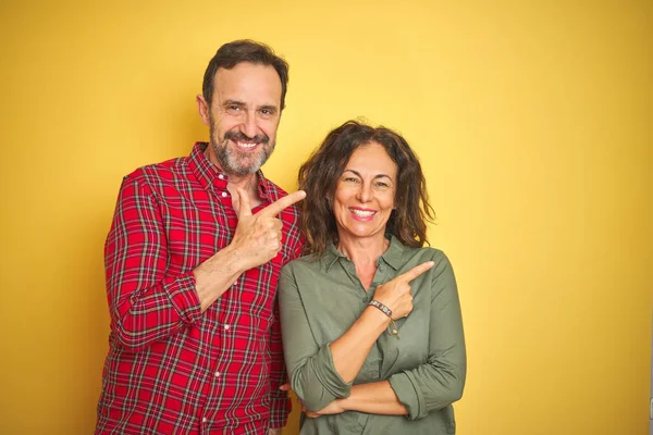 Yüzünde mutlu ve doğal ifade ile yan kadar el ve parmak ile işaret yüz bir gülümseme ile izole sarı arka plan neşeli üzerinde güzel orta yaş çift