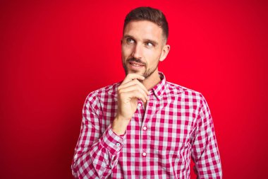 Kırmızı izole arka plan üzerinde genç yakışıklı adam çene üzerinde soru, dalgın ifade düşünme el ile. Gülümseyen ve düşünceli bir yüz. Şüphe kavramı.