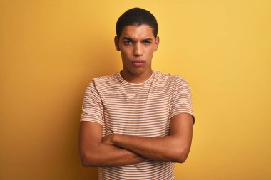 Genç yakışıklı Arap adam çizgili t-shirt izole sarı arka plan şüpheci ve sinirli, çapraz kolları ile yüzünde onaylamayan ifade üzerinde duran giyiyor. Negatif kişi.